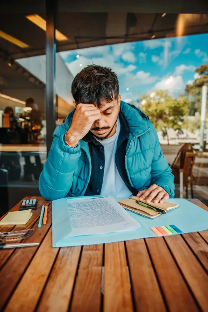 A person sits at an outdoor table reading documents, appearing focused and thoughtful, with pens, sticky notes, and a calculator nearby—perhaps preparing for a psychological assessment Mississauga or reviewing psychoeducational assessment results.