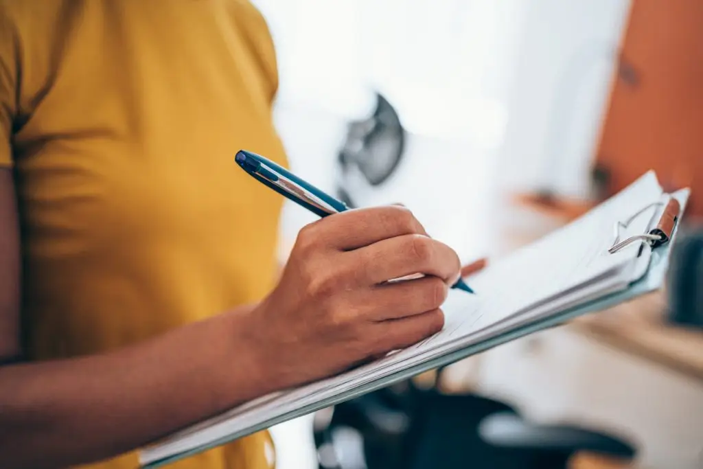 A person in a yellow shirt holds a pen and writes on a clipboard with documents, possibly related to psychoeducational assessment Mississauga or adult ADHD assessment and diagnosis.